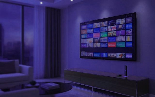 A living-room TV showing an IPTV channel guide with a streaming stick on the console